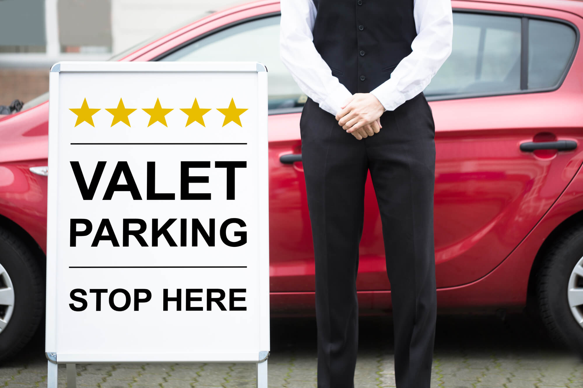 Valet attendant standing beside a Valet Parking Stop Here sign