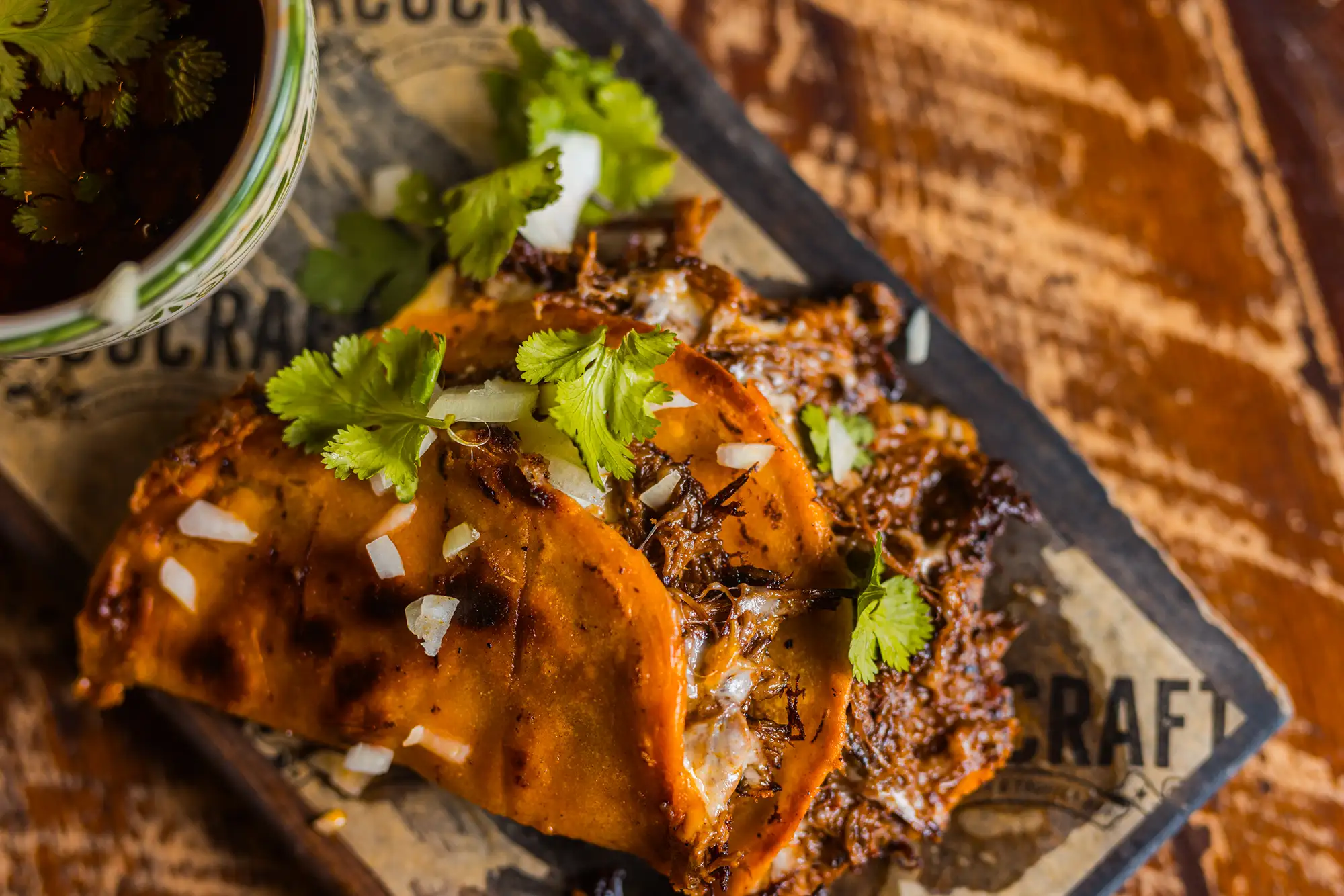 Birria tacos topped with cilantro and onion at Tacocraft