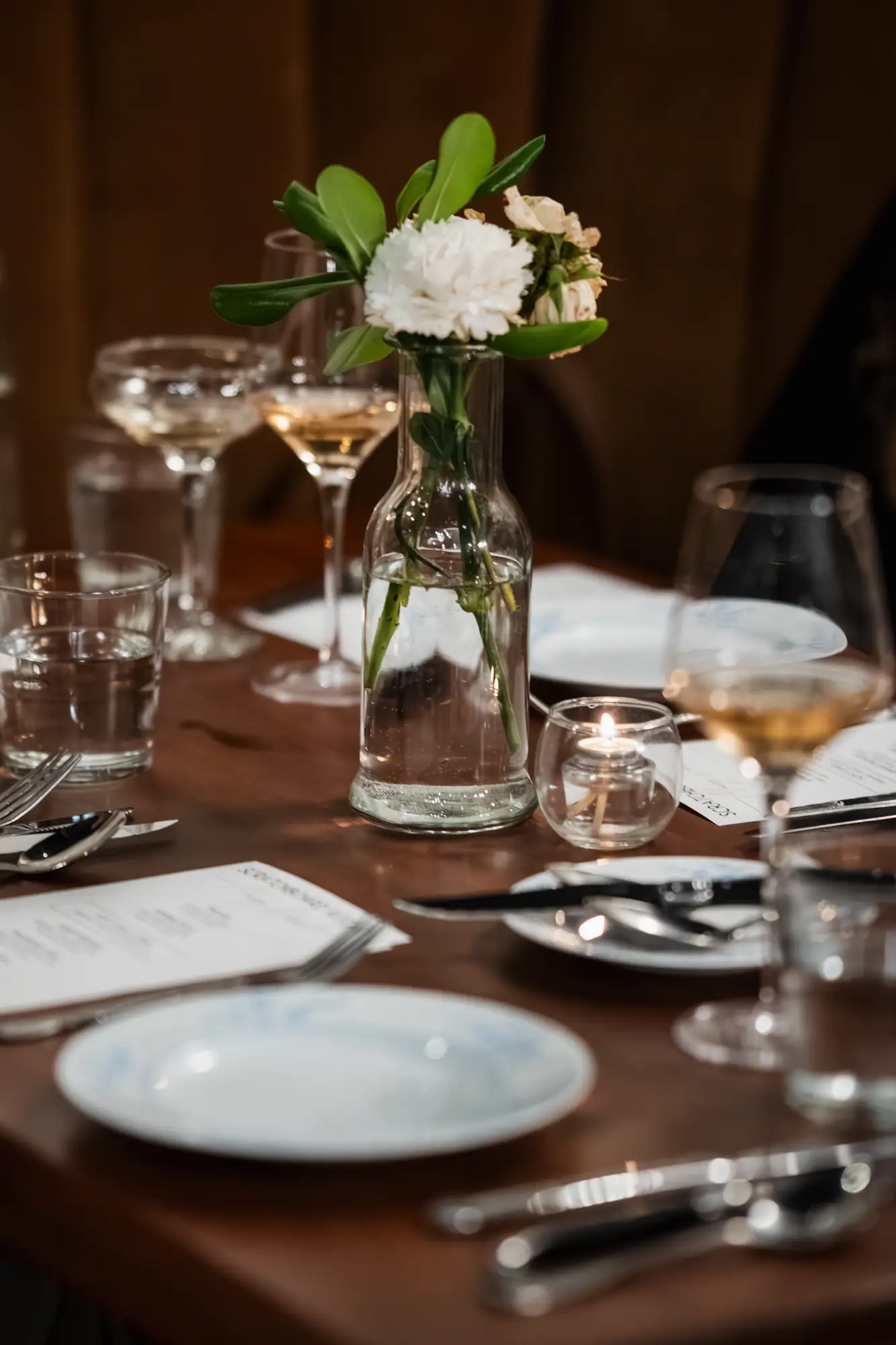 A candlelit dinner table at Scratchboard Kitchen with a carnation and glasses of white wine